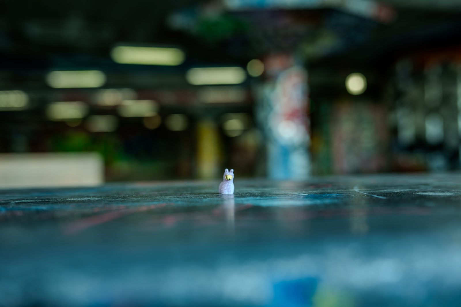 The plastic llama alone on the teal-painted floor of an empty multi-storey car park, rows of pillars blurred behind.