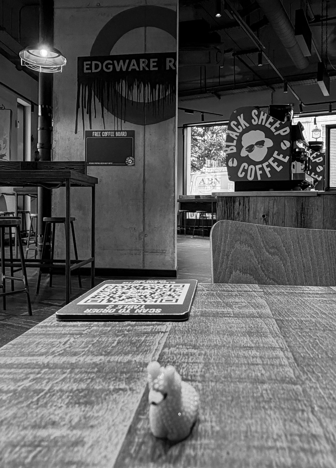 A small plastic llama sits on the tiled floor of a London Underground platform, the Edgware Road roundel on the wall behind it, in black and white.