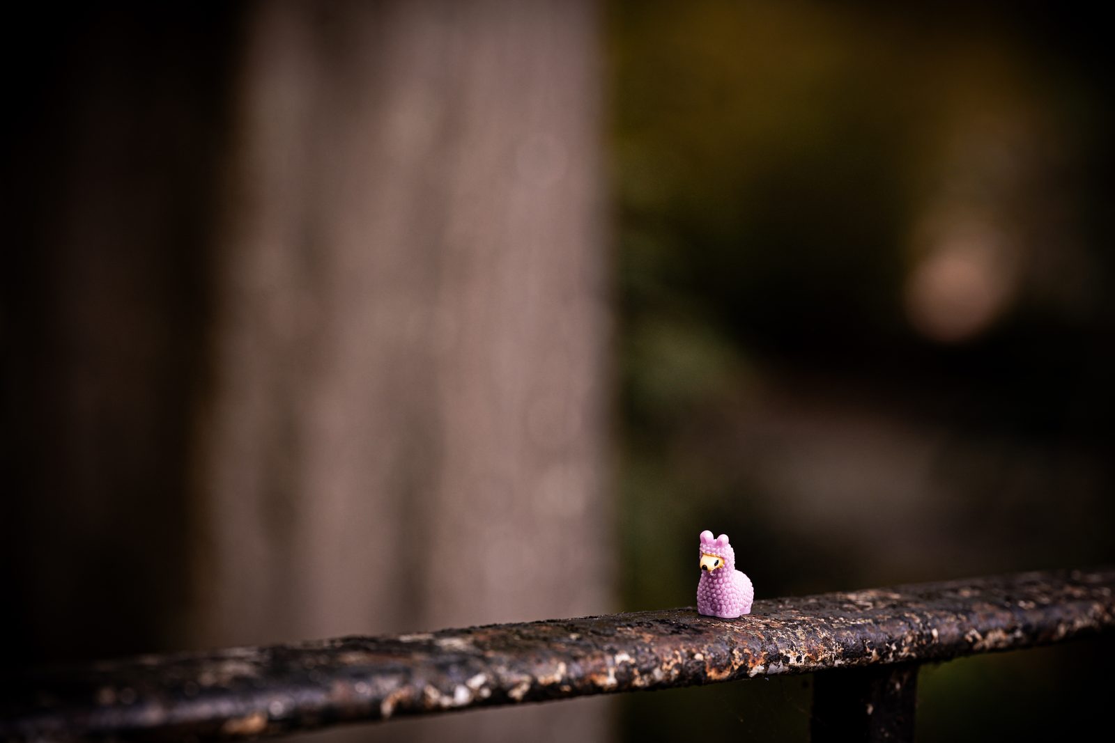 The plastic llama on a rusted metal rail with out-of-focus woodland behind.